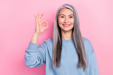 Photo of shiny sweet retired woman blue sweater smiling showing okey sign isolated pink color background