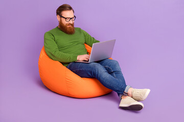 Full body photo of handsome intelligent guy sitting bag use wireless netbook isolated on violet...