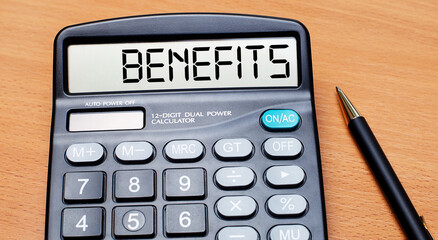On a wooden table there is a black pen and a calculator with the text BENEFITS. Business concept