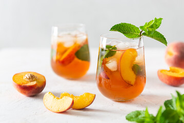 Fresh Peach iced tea. Iced tea with peach slices, mint and ice cubes on a white background. Close up. Homemade refreshing summer drink recipe. Refreshing peach lemonade. Summer cold drink