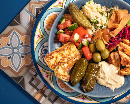 Loaded sharing portion of traditional Mediterranean Arabic food of hummus, olives, grilled chicken, halloumi, dolma, couscous, salad and pickles