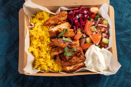 Traditional Eastern Mediterranean takeaway meal of grilled chicken, yellow rice, fresh salad and yoghurt in cardboard