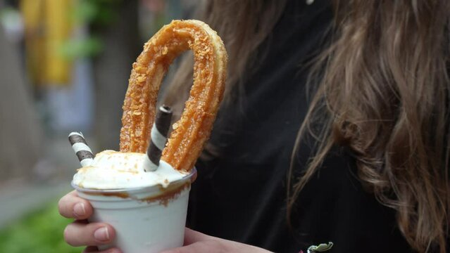 Close up showing girl holding a tempting glass of churro milkshake standing outdoors.