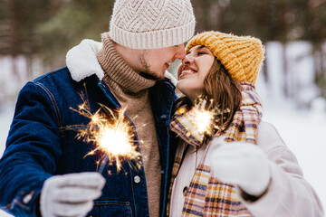 people, christmas and holidays concept - happy smiling couple with sparklers in winter forest