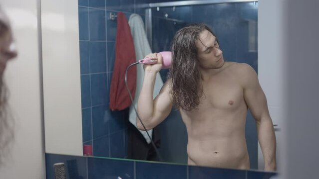 Completely naked metrosexual man using a hair dryer in front of the bathroom mirror after a shower - Middle shot