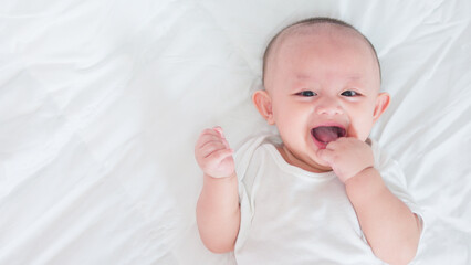 Portrait of cute asian newborn baby lying play on white bed look at camera with laughing smile happy face. Innocent little new infant adorable. Parenthood and Mother Day concept.