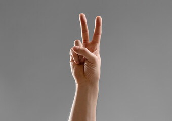 gesture, count and people concept - close up of male hand showing peace over grey background