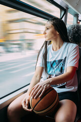 Young woman basketball player sit on a bus with your ball on your legs while she watches the city...