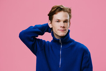 handsome, attractive guy posing on a pink background in a blue sweater with his hand behind his head
