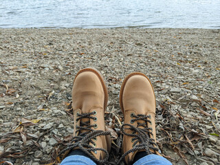 Girl feet in beige boots sitting on the river shore relaxing and enjoying the view and nature calm.