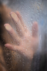 Female hand and unrecognizable silhouette behind wet glass in shower