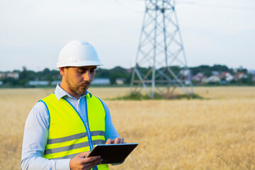 Fototapeta premium a male engineer in a helmet and goggles uses a smartphone for field work near a telecommunications tower that controls cellular electrical installations.