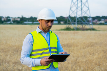 Fototapeta premium a male engineer in a helmet and goggles uses a smartphone for field work near a telecommunications tower that controls cellular electrical installations.