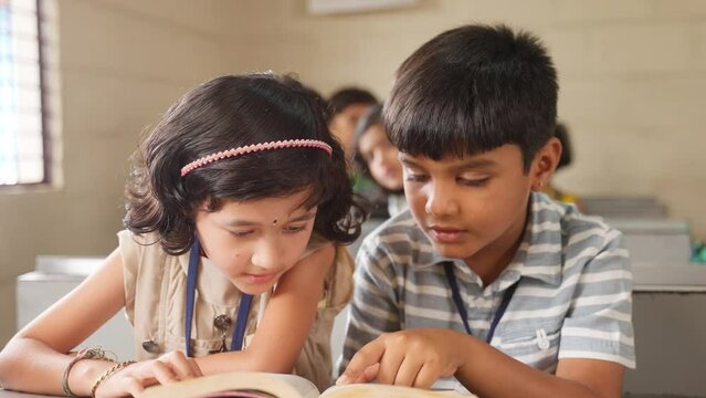 Teenage kids studying for examination while sitting on desk at classroom by sharing book - concept of education, freindship and knowledge