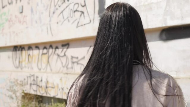 A young beautiful Caucasian woman turns around and looks at the camera - closeup - a wall with graffiti in the background