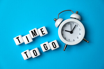 Business and lifestyle concept. On the blue surface there is a white alarm clock and cubes with the inscription - Time to Go.