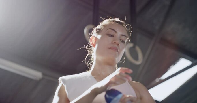 Active young woman drinking water during a break from exercise in a gym from below. Sweaty and exhausted athlete quenching her thirst and cooling down after a challenging workout in a fitness center