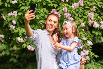 family, motherhood and people concept - happy mother and little daughter with smartphone taking selfie at summer park or garden