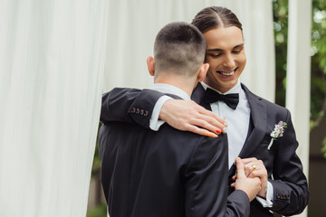 happy gay couple in suits holding hands and hugging on wedding day.