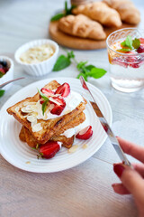 Woman hand eating breakfast of french toast with strawberries and maple syrup, good morning..