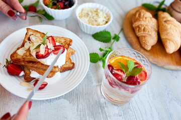 Woman hand eating breakfast of french toast with strawberries and maple syrup, good morning..