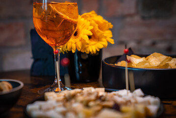 Traditional italian aperitif with cheese, nuts and aperol spritz drink on the wooden table with blurred food on the background in a bar