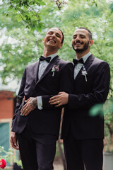 low angle view of happy gay newlyweds in formal wear with boutonnieres and golden rings.
