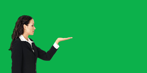 Profile side of beautiful businesswoman showing something or copy spase for product. Brunette woman looking at her hand in business studio concept, isolated on vivid green background.