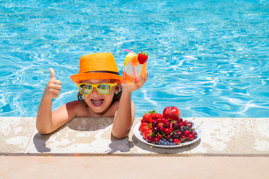 Child Drink Cocktail. Summer Child By The Pool Eating Fruit And Drinking Lemonade Cocktail. Summer Kids Vacation Concept. Little Kid Boy Relaxing In A Pool Having Fun During Summer Vacation.