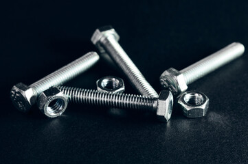 Several bolts and nuts lie on a black surface, this fastener is silver in color, photographed close-up, fastener still life