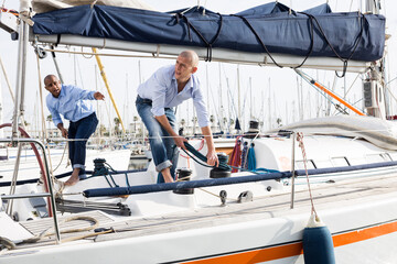 A couple of guys in blue shirts and jeans working on private sailing yacht in seaport