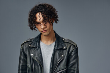 Fototapeta na wymiar Self-confident stylish tanned curly man leather jacket looks at camera posing isolated on over gray studio background. Cool fashion offer. Huge Seasonal Sale New Collection concept. Copy space for ad