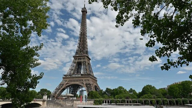 Paris, France. June 2022. Amazing footage of the Eiffel Tower in a postcard image: the crowns of the trees frame it while the white clouds roll across the blue sky.