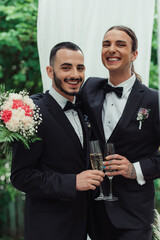 happy gay couple in suits holding glasses of champagne on wedding day.