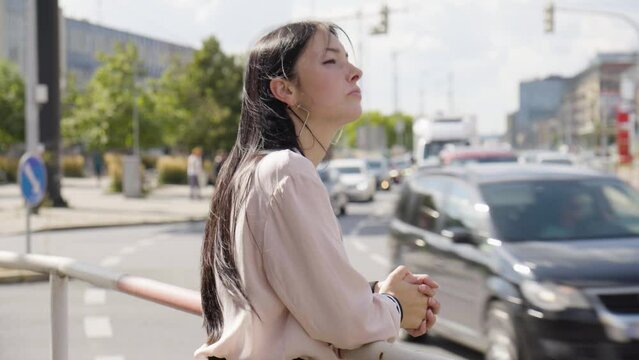 A young beautiful Caucasian woman thinks about something in an urban area - a busy road in the background