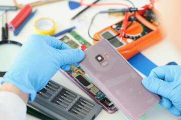 Technician repairs broken smartphone at table in workshop