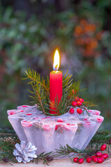 Winter-Gartendekoration mit Eislaterne, Berberitzen und roter Kerze	
