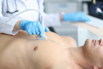 Doctor holding ultrasound machine on man chest in clinic