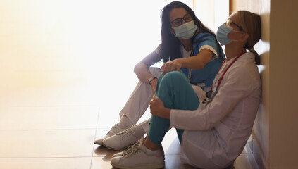 Surgeon in hospital corridor with communicates with doctor sitting on floor