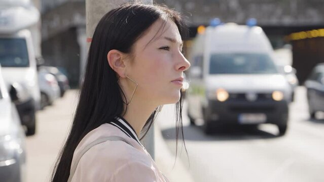 A young beautiful Caucasian woman thinks about something in an urban area - closeup - a busy road in the blurry background