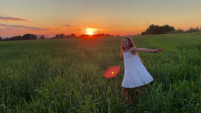 girl dancing in the field. happy childhood family friendship concept. a little girl with long dark hair is spinning in a white dress in wheat, a girl is dancing at sunset in a field