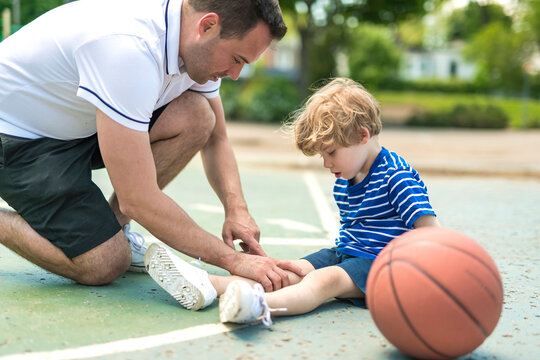 portrait of focused adult man coach helping boy with knee trauma after playing basketball on the court