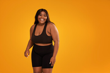 Happy plus size woman posing in sporty black fashionable clothes, smiling to the camera. Sports and...