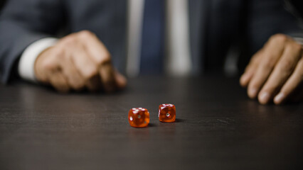 Businessman throwing pair of red dice on table, gambling, hobby for rich