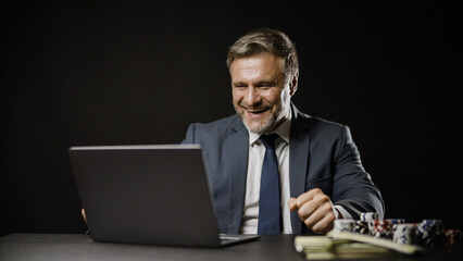 Excited businessman gambling online using laptop and winning, celebrating his luck