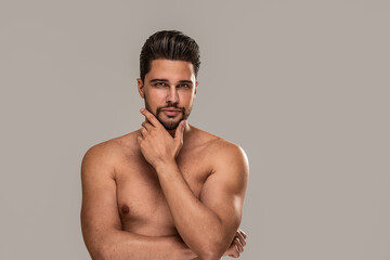 Fototapeta premium Handsome sexy man with brown eyes posing shirtless on grey studio background. Muscular body. Skin care.