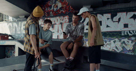 Cheerful friends watching video on mobile phone at skate park with graffiti.