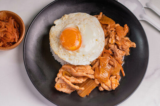 Stir-fried pork with kimchi and fried egg in a black plate. Korean food.