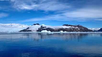 Icebergs floating at the base of a snow covered mountain, in the Southern Ocean, at Cierva Cove, Antarctica