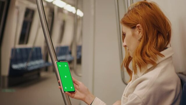 Side view female watching green screen phone in the subway train. Social Network. Work and Travel. New Apps. Phone User. Smartphone with Green Screen Mock Up Display.